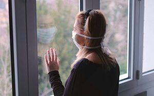 woman with face mask looking out a window