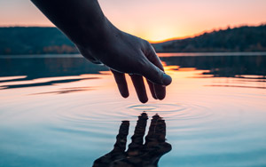 a hand touching water creating a gentle ripple